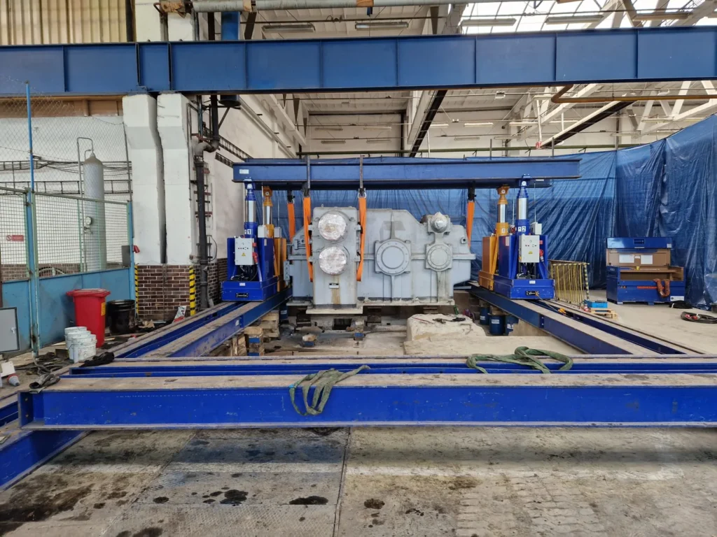 Großes Anlagenbauteil zwischen zwei blauen Hubsystemen in der Montagehalle